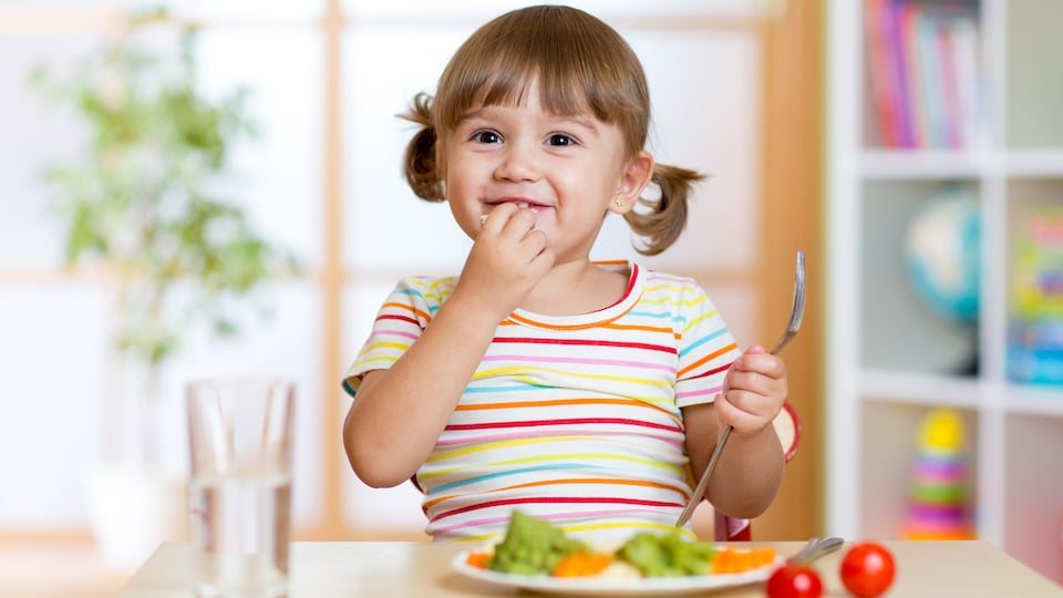 Une fillette mange des légumes avec le sourire.