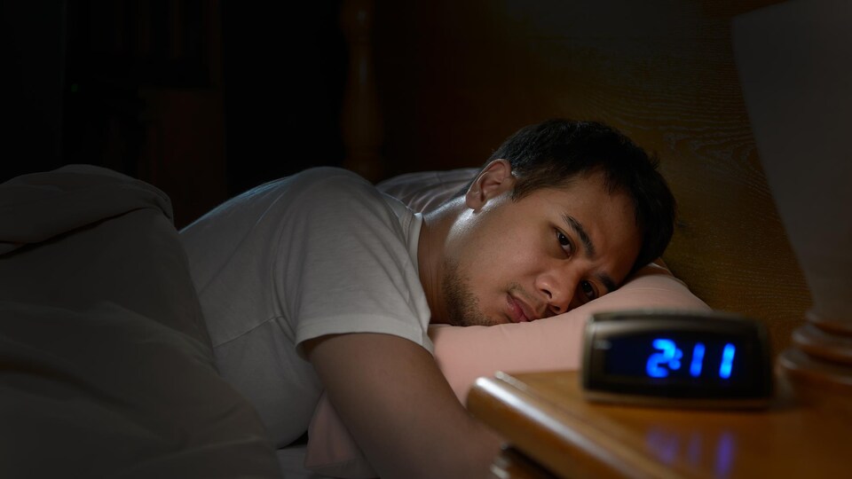 Un homme souffrant d'insomnie regarde mélancoliquement son réveil depuis son lit.