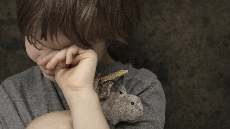Un enfant s'essuie les yeux en serrant un animal en peluche contre lui.