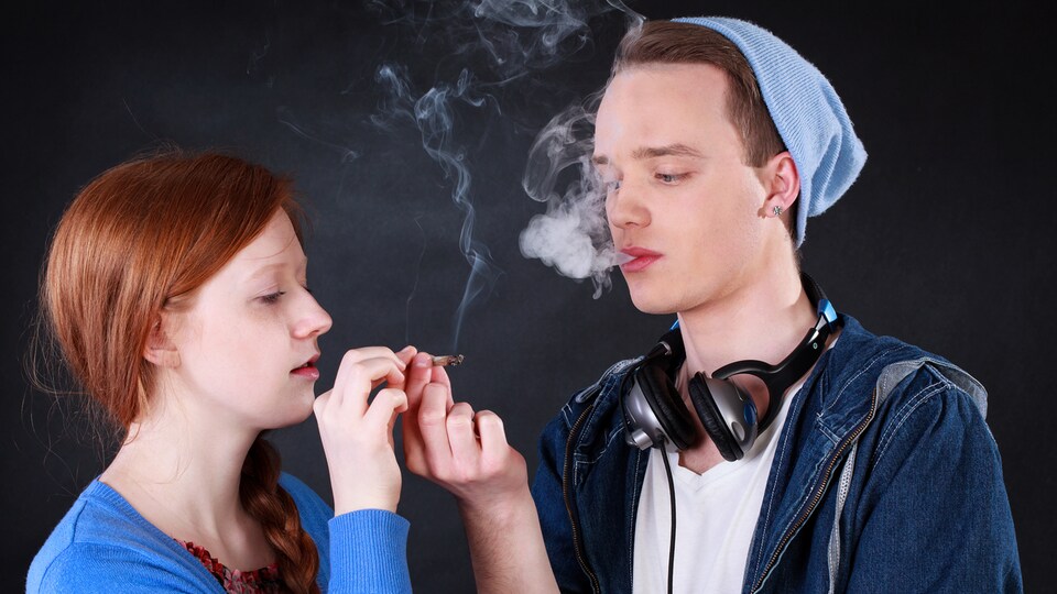 Une jeune fille et un jeune garçon s'échangent un joint de cannabis.