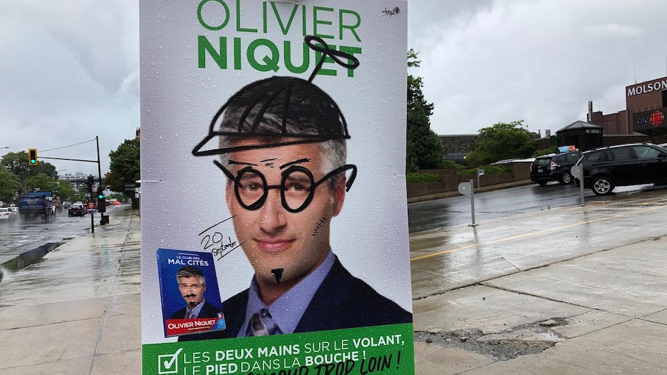 On voit Olivier Niquet avec une casquette dessinée et des lunettes, les deux dernières lettres de son nom de famille sont barrées.