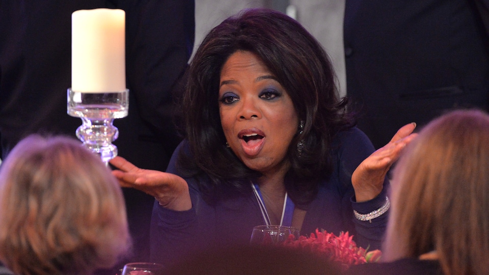 Oprah Winfrey, assise à une table, hausse les épaules lors d'un dîner d'honneur à la Maison-Blanche, en 2013.