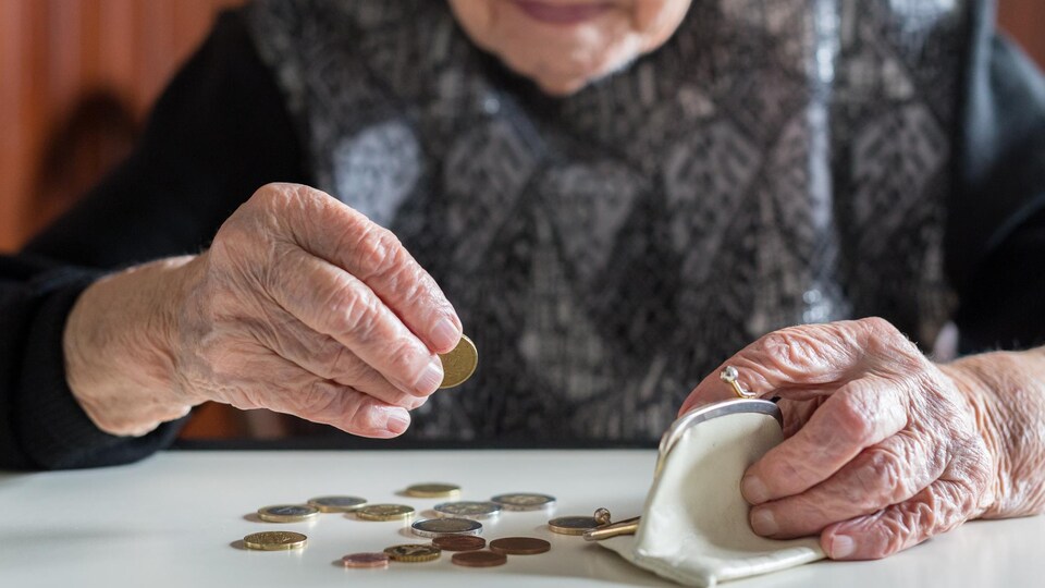 Un dame âgée compte ses sous, posés sur une table devant elle.