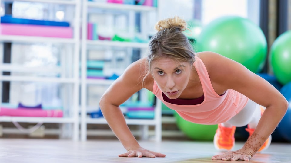 Une jeune femme fait des push-ups dans un gymnase.