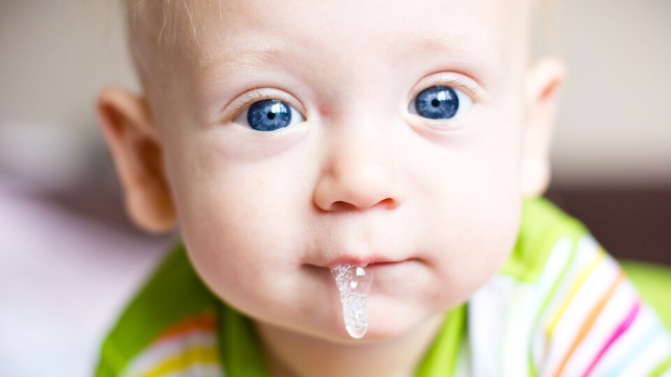 De grosses gouttes de salive coulent de la bouche d'un bébé blond.