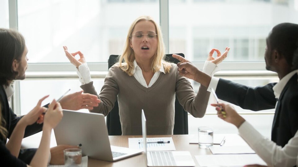 Une femme stressée mime la méditation depuis son bureau, au travail.