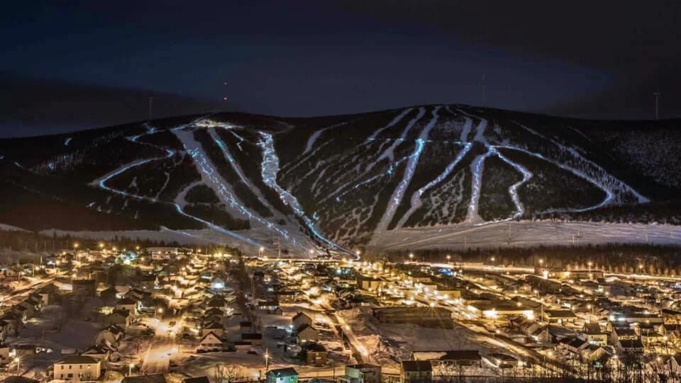 Un village éclairé au pied de montagne avec des pistes de skis lumineuses.