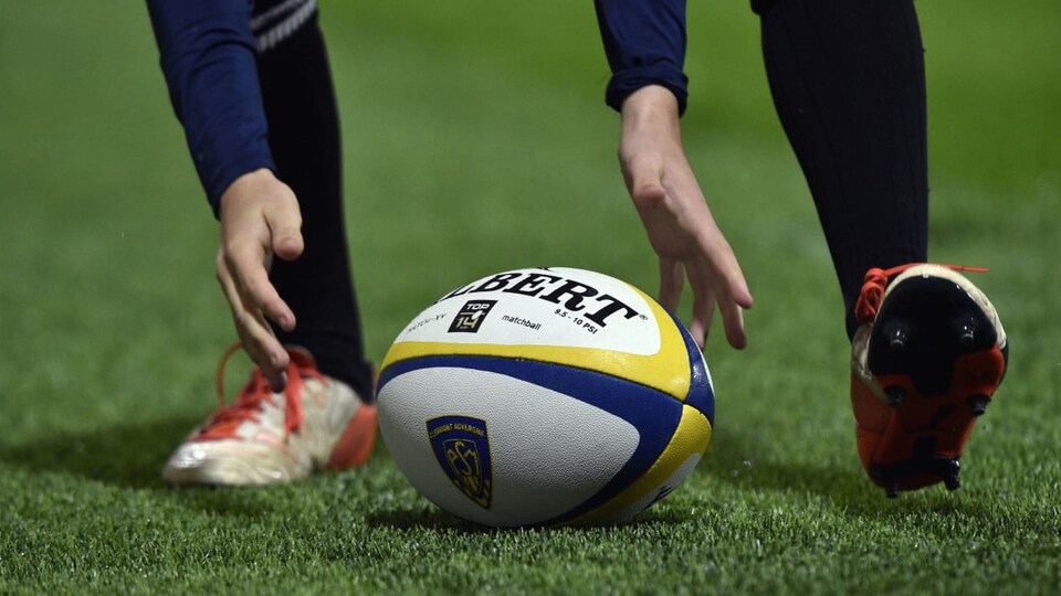 Un homme prend un ballon de rugby dans ses mains.