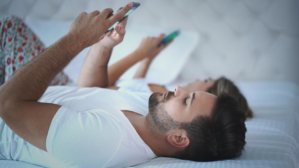 Un homme et une femme consultent leur téléphone au lit.