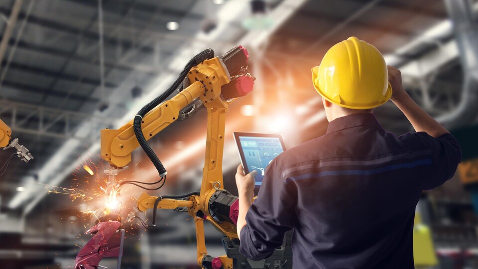 Une tâche est effectuée par un robot dans une usine, sous le regard d'un employé.