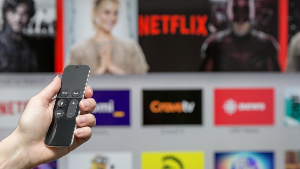 Une personne, télécommande à la main, s'apprête à utiliser la chaîne de diffusion en continu Netflix, dont on voit le logo sur un grand écran.