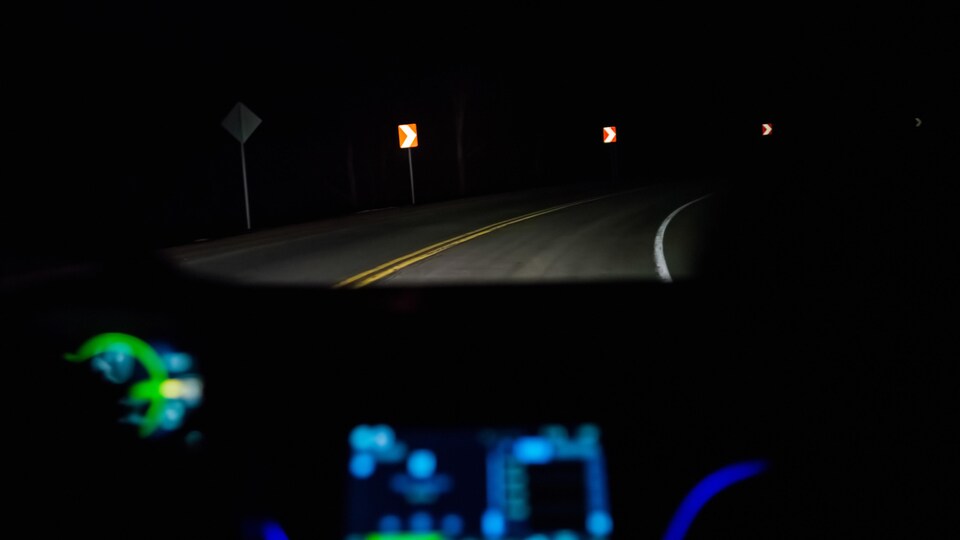 La vue d'une route la nuit, de l'intérieur d'une automobile.