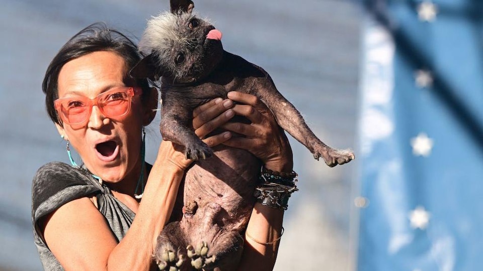 Jeneda Benally réagit de manière heureuse et surprise en tenant son chien, un chinois à crête de 17 ans, sans ses bras.