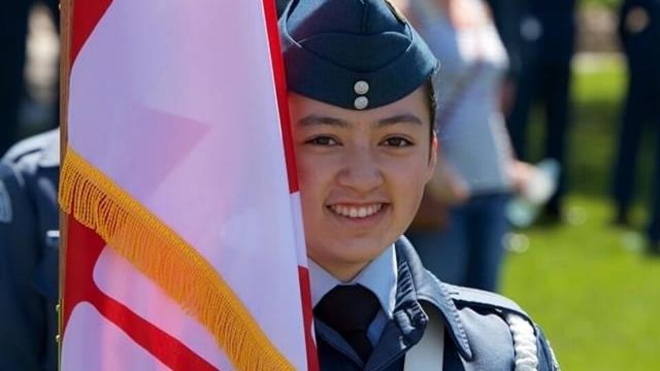 Une jeune fille en uniforme de cadète derrière un drapeau.