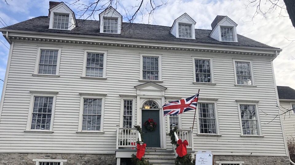 Vieille maison avec des déclins et quatre fenêtres au toît et un drapeau britannique qui flotte devant la porte d'entrée.