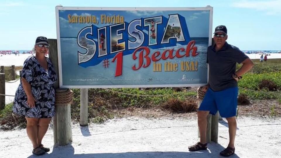 Un couple de voyageurs retraité autour d'une affiche d'une plage floridienne.