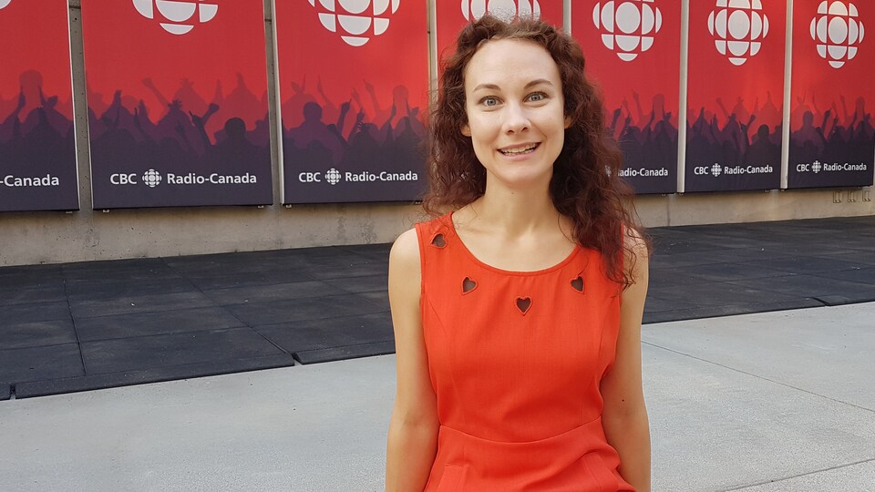 La harpiste Mylle Fournier assise sur le béton devant des affiches de Radio-Canada