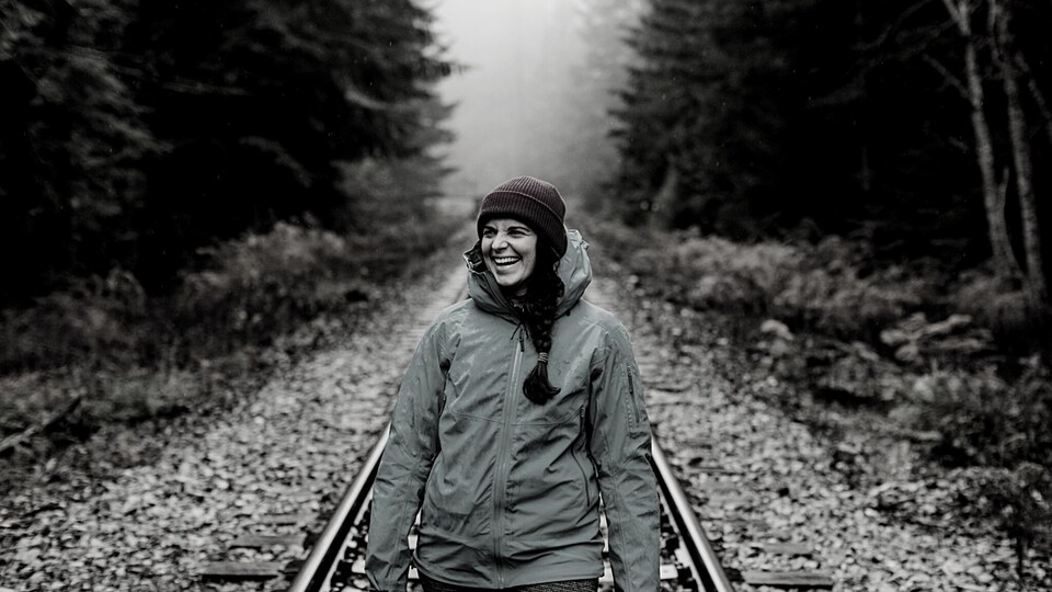 Camille-Alexie Chalifoux marchant sur un rail de chemin de fer dans un paysage forestier.