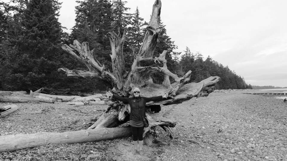 Sylvie Cockburn pose devant la racine d'un arbre géant échoué sur une plage.