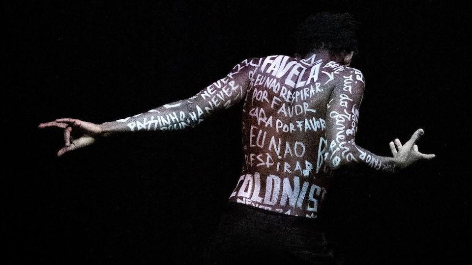 Un homme noir danse. De nombreux noms de personnes sont inscrits en blanc sur son dos nu.