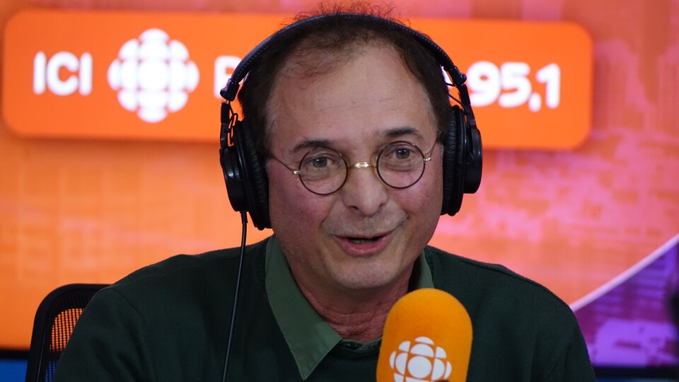 Normand Baillargeon derrière un micro dans un studio radio de Radio-Canada.