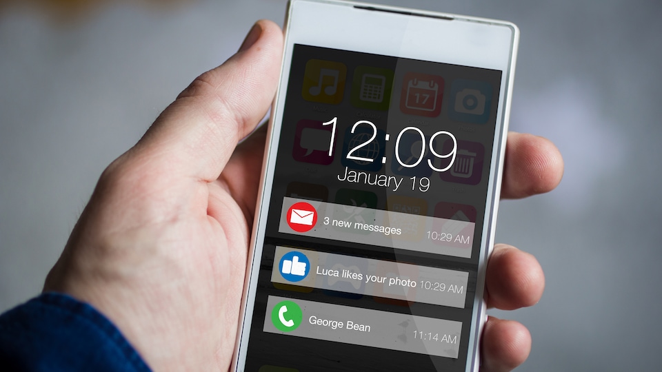 Une main tenant un téléphone intelligent dont l'écran affiche trois notifications.