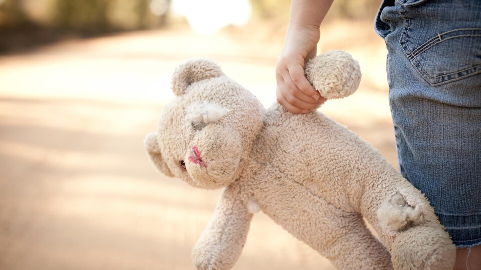 Une vieille peluche dans la main d'un enfant qui marche.