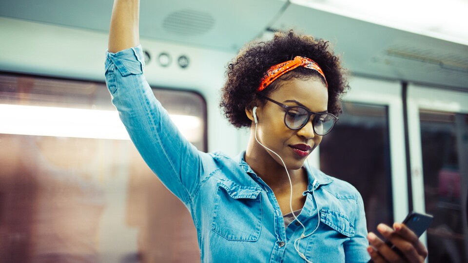 Une jeune femme écoute un balado dans le métro.