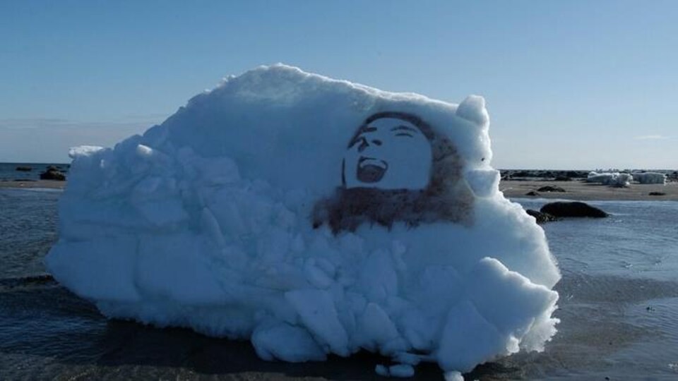 Une oeuvre (illustrant le visage d'un homme, la bouche ouverte) du Collectif de la dérive sur un morceau de neige, sur une plage nord-côtière.