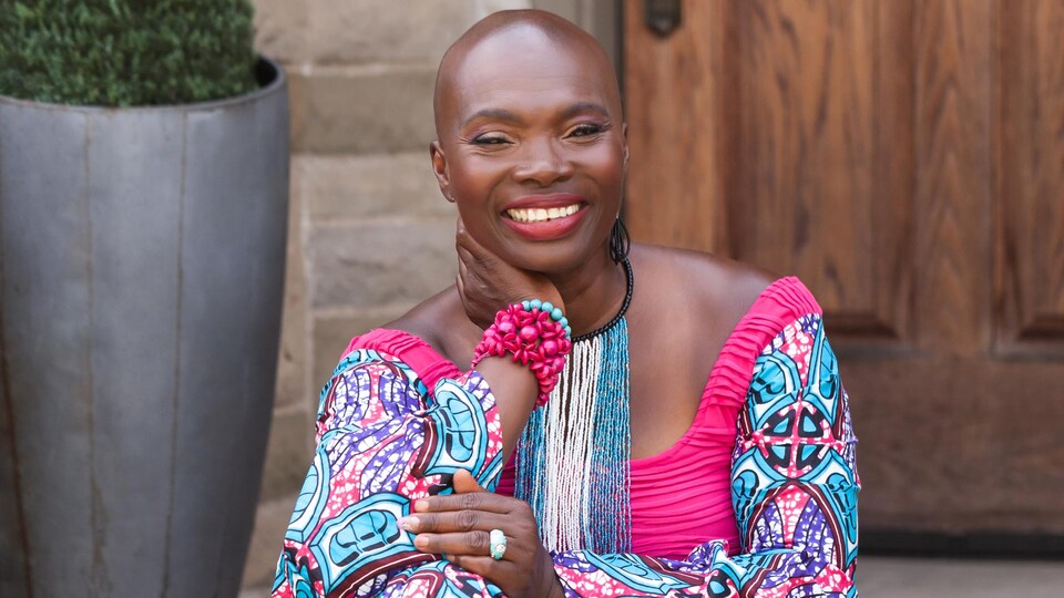 Une femme noire souriante vêtue d'une robe bleu et rose.