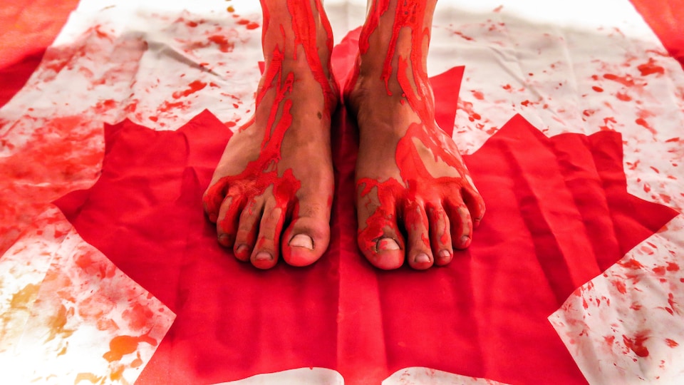 Un drapeau canadien piétiné, maculé de peinture rouge, qui représente le sang.