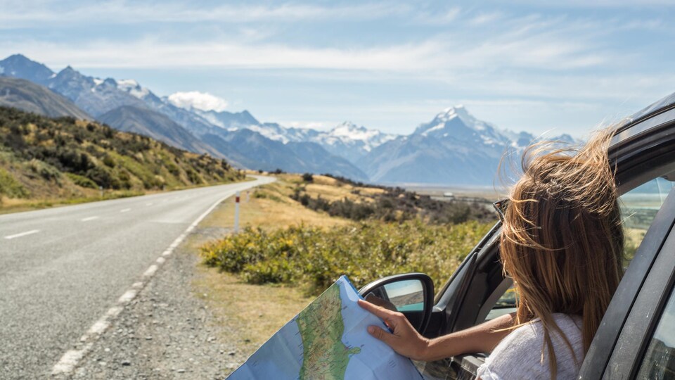 Portrait of a young woman in a car looking at a map for directions.