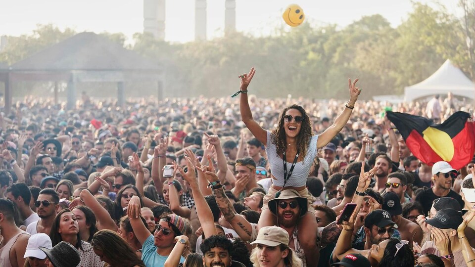 Photo d'une foule en plein concert extérier avec des gens levant les bras dans les airs.