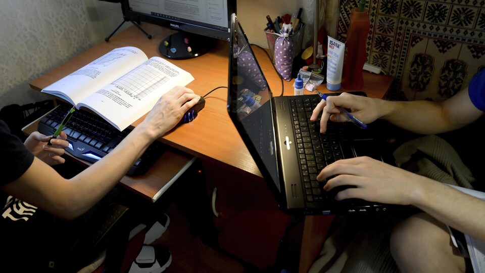 Des adolescents dont on distingue juste les avant bras étudient à la maison sur leurs ordinateurs.