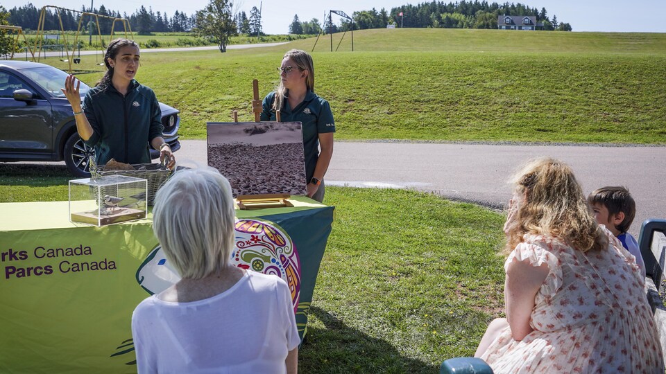 Des personnes assises devant un stand de Parcs Canada, animé par deux personnes.