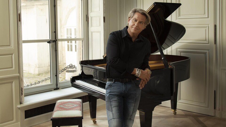 Accoudé sur un piano, Alain Lefèvre regarde la caméra.
