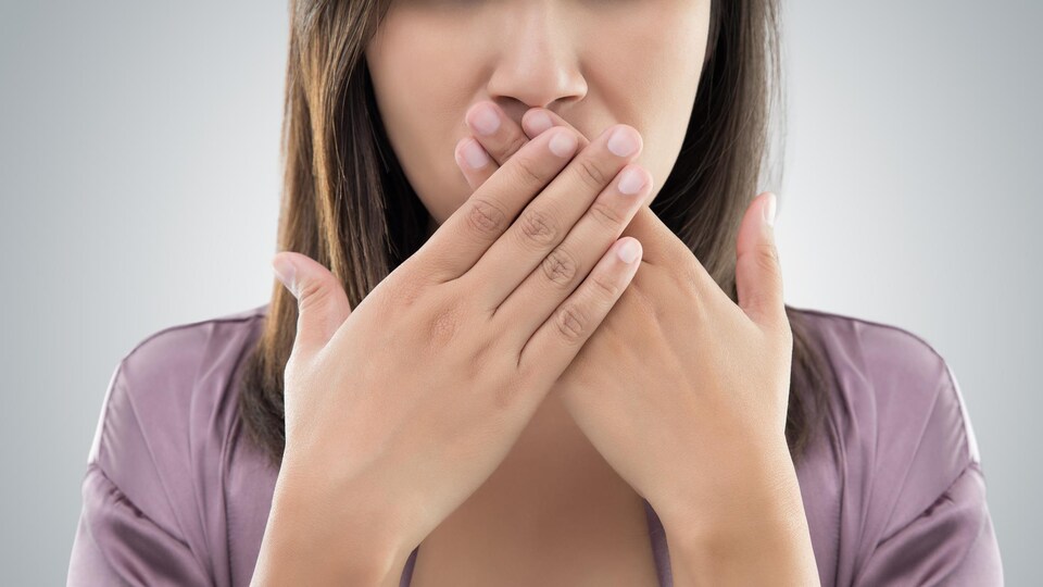 Une femme tient ses deux mains croisées sur sa bouche.