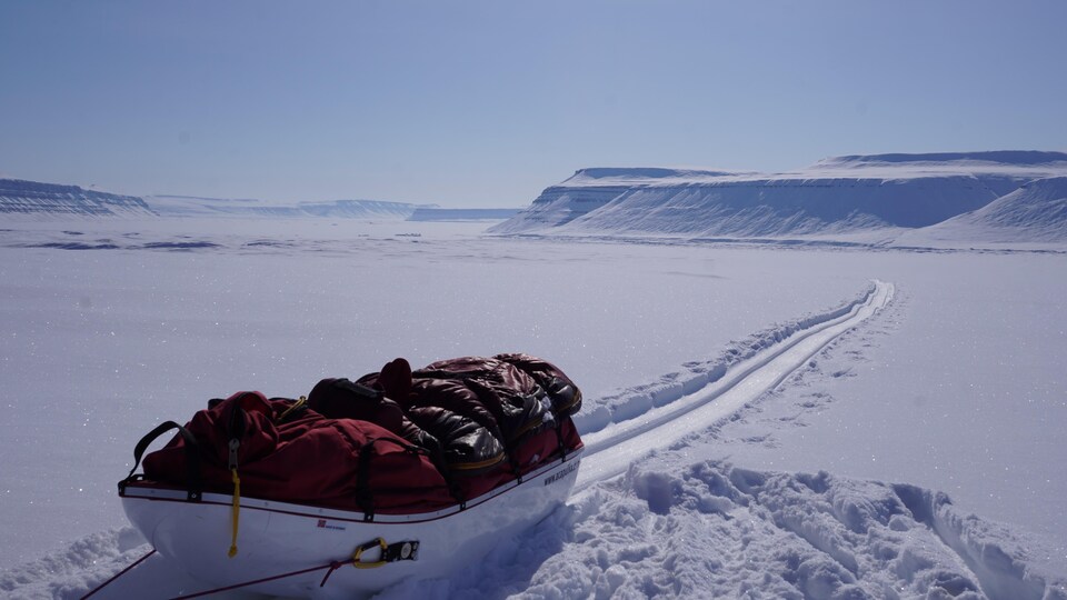 Un grand traîneau rempli d'équipement sur une vaste étendue de neige à perte de vue. 