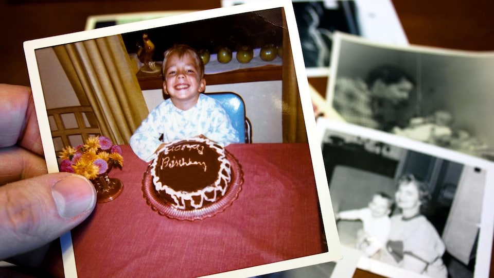Gros plan d'une main qui tient une photo sur laquelle un petit garçon pose devant un gâteau de fête.
