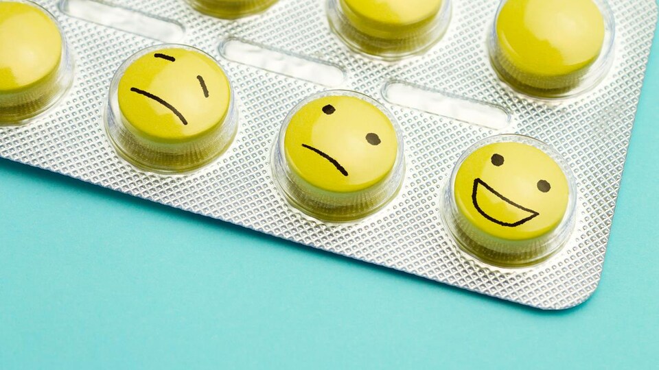 Des faces de bonhommes tristes, confus et heureux sont dessinées sur des pilules.