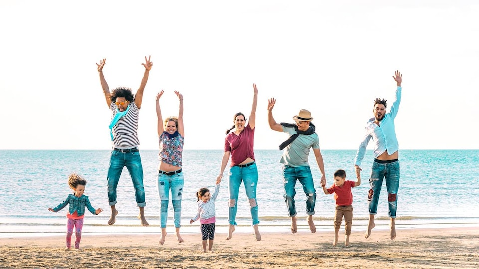 Un groupe de cinq adultes et trois enfants sautent sur une plage. 