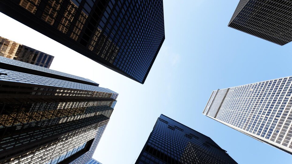 Vue en contre-plongée de cinq hauts immeubles qui se découpent sur un ciel bleu immaculé.