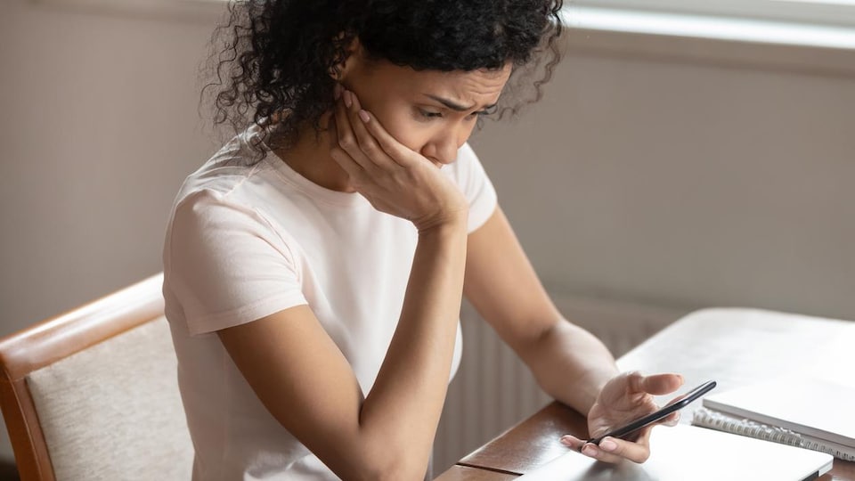 Une femme consulte son téléphone cellulaire avec un air contrarié.