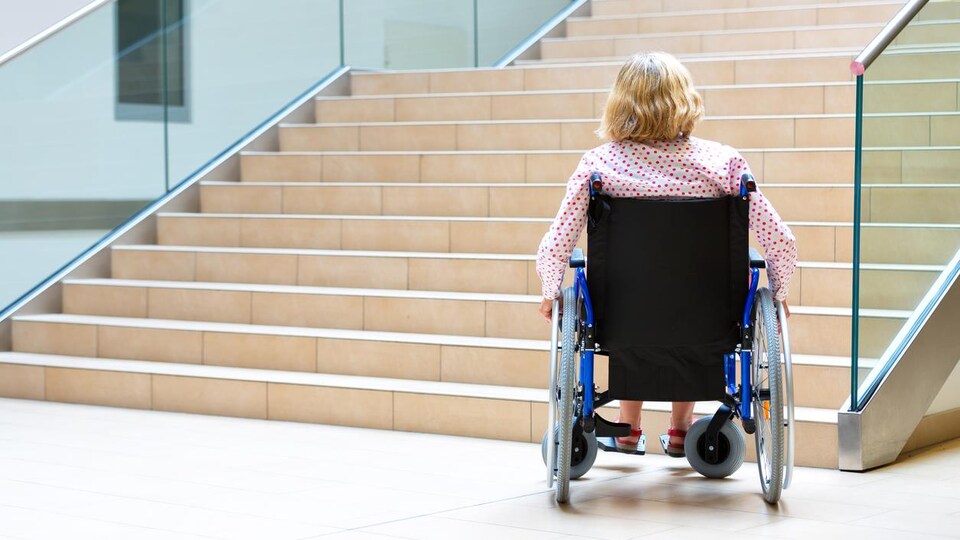 Une femme dans une chaise roulante se trouve en bas des marches d'un grand escalier.