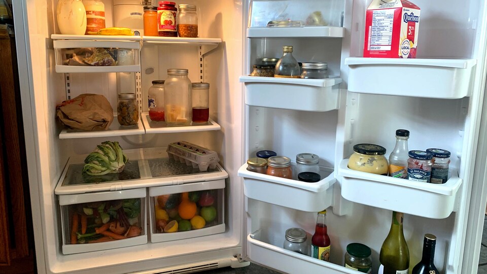 L'intérieur d'un frigo ouvert qui contient des fruits, des légumes et des contenants en verre.