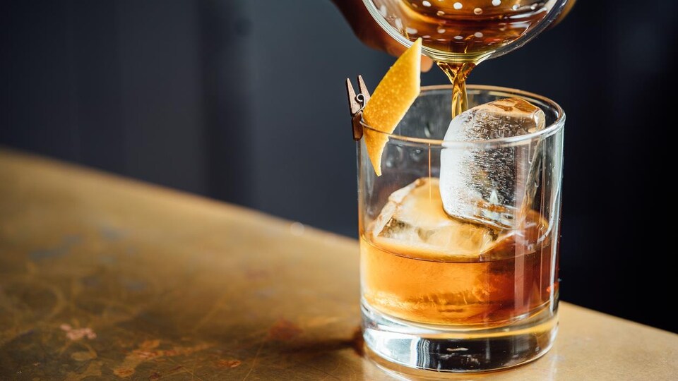 Photo d'un cocktail versé dans un verre avec de la glace et une pelure d'orange.