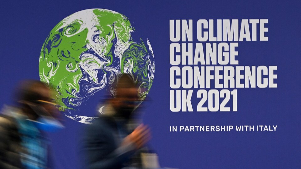 Deux personnes passent devant une affiche de la Conférence de Glasgow sur les changements climatiques. 