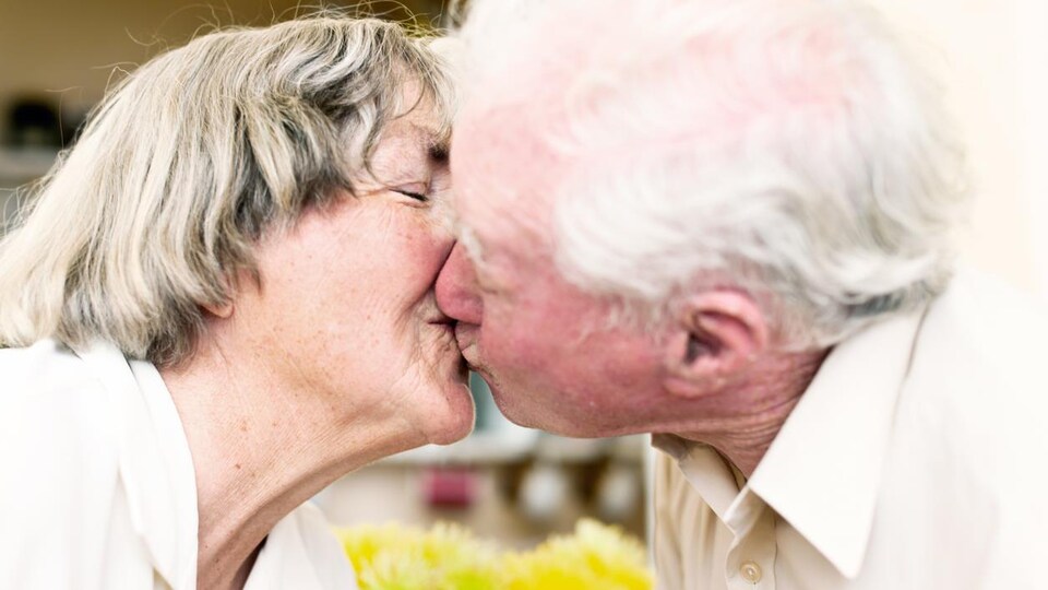 Une femme et un homme aînés se donnent un bisou sur la bouche.