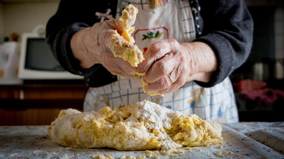 Gros plan sur les mains pleines de pâte d'une vieille dame qui prépare des pâtes fraîches.