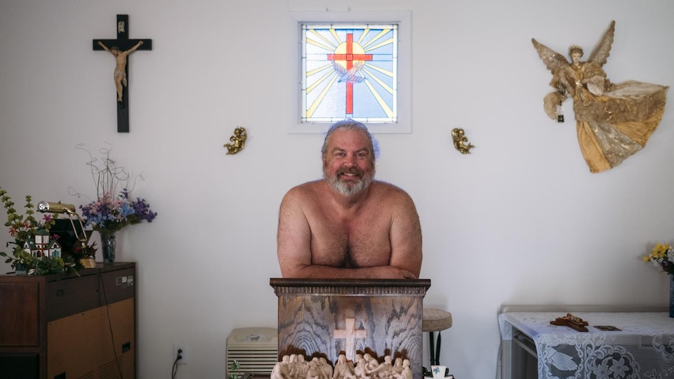 Photo d'un homme torse nu derrière un pupitre dans une petite église.